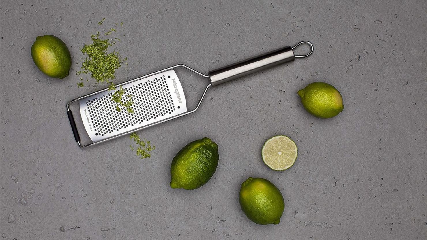 Professional grater on grey countertop surrounded by five limes, one slightly grated.