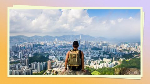 A photo of a person sitting a mountain overlooking a city with a large backpack on their back