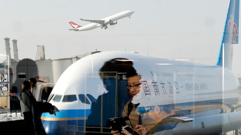 Passengers walk past a couple browsing their smartphones near an Airbus A380 passenger airplane, owned by China Southern Airlines, parked on the tarmac at the Beijing Capital International Airport, on November 19, 2016.