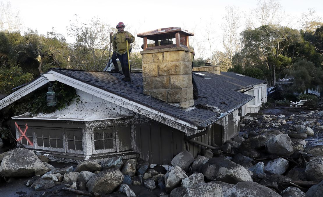 A firefighter stands on the roof of a house buried under mud and rocks following a landslide in Montecito, California, in 2018.