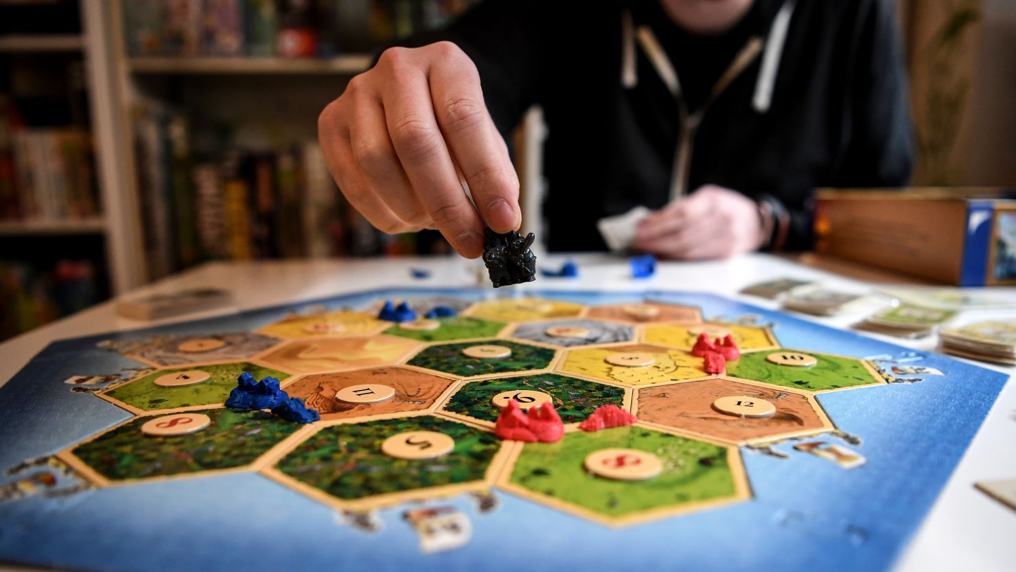 A player places one of their game pieces on the board in CATAN.