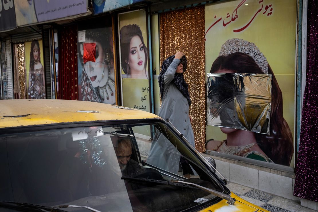 An Afghan woman walks past beauty salons with defaced window decorations, in Kabul, Afghanistan, on Sunday, Sept. 12, 2021.