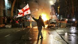 A man waves a Georgian national flag in front of a burning barricade as other protesters stand behind not far from the Georgian parliament building in Tbilisi, Georgia, Thursday, March 9, 2023. Police in Georgia's capital have fired water cannon and tear-gas to disperse demonstrators around the parliament building protesting a draft law aimed at curbing the influence of "foreign agents", among fears it could be used to silence oppositions. (AP Photo/Zurab Tsertsvadze)