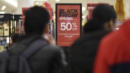 People walk past advertised Black Friday discount signs at the Macy's retail store inside the Queens Center Mall, New York, NY, November 24, 2023.