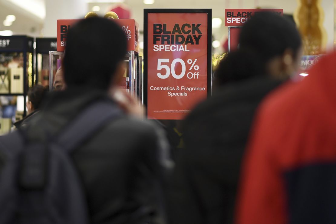 People walk past advertised Black Friday discount signs at the Macy's retail store inside the Queens Center Mall, New York, NY, on November 24, 2023.