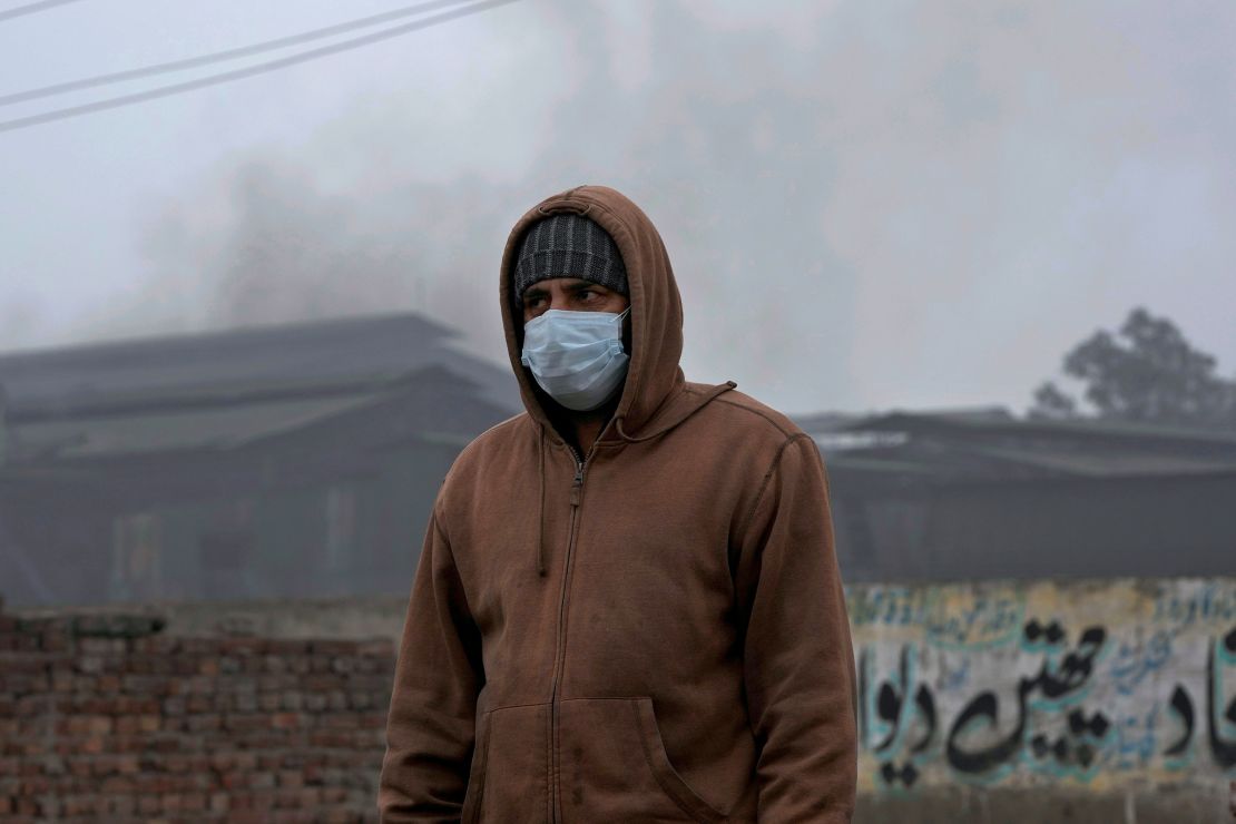 A man wears a mask as he walks past a small iron factory in Lahore, Pakistan, on January 16, 2024.