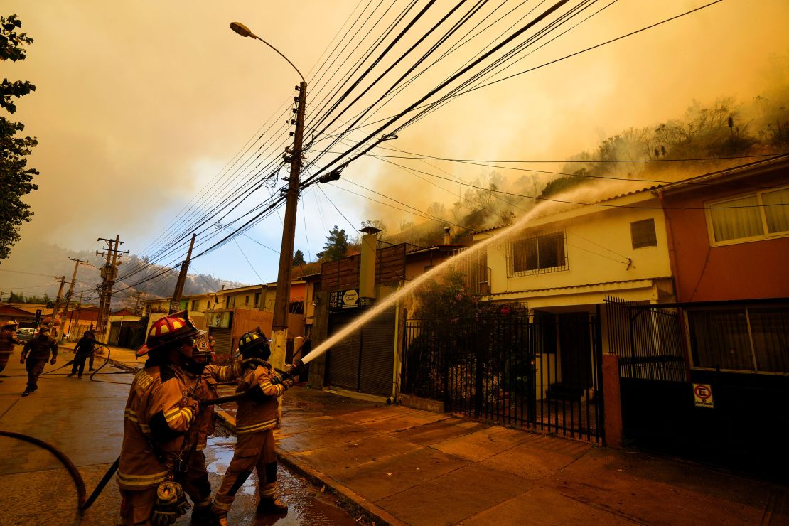 Firefighters protectively spray water on homes as forest fires burn nearby.