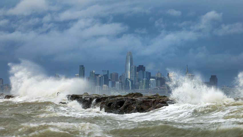 Waves crash over a breakwater in Alameda, Calif., with the San Francisco skyline in the background on Sunday, Feb. 4, 2024. High winds and heavy rainfall are impacting the region.
