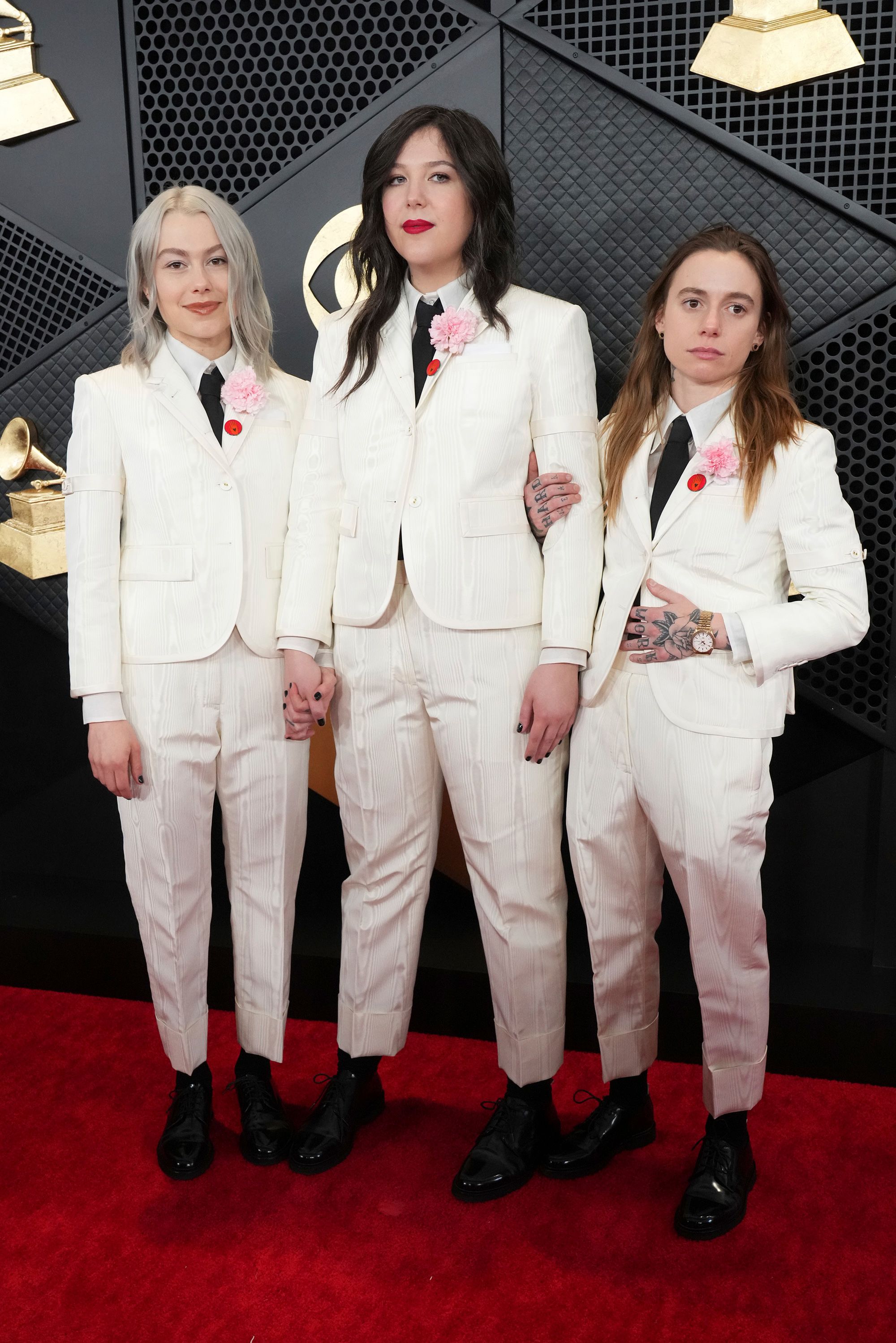 From left: Phoebe Bridgers, Lucy Dacus and Julien Baker of Boygenius in matching cream-colored Thom Browne suits with red pins and carnations on their lapels.