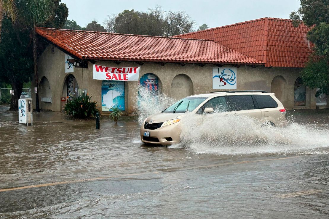 A vehicle drives through water on a flooded street in Ventura, California.