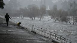 A man walks his dog on the edge of the Los Angeles River, carrying stormwater downstream Sunday, Feb. 4, 2024, in Los Angeles. The second of back-to-back atmospheric rivers battered California, flooding roadways and knocking out power to hundreds of thousands and prompting a rare warning for hurricane-force winds as the state braced for what could be days of heavy rains.
