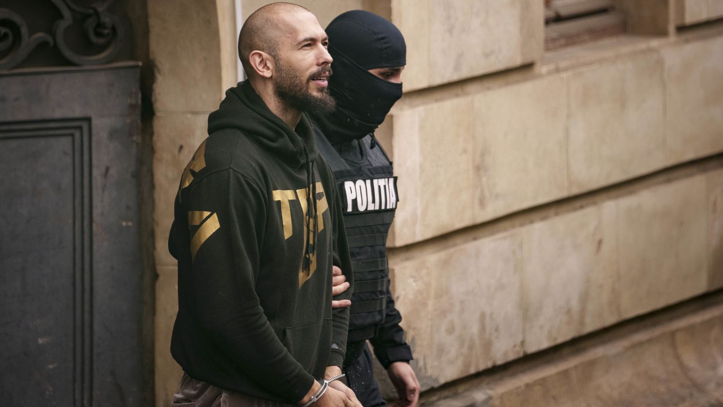 A police officer escorts Andrew Tate, left, from the Court of Appeal in Bucharest on Tuesday.