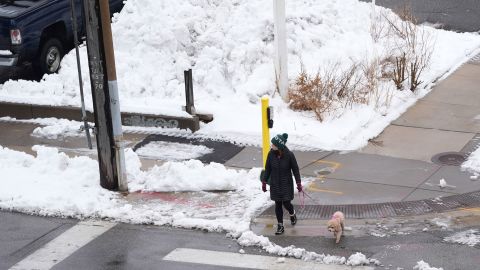 A pedestrian with a dog crosses the street near a large pile of snow Monday, March 25, 2024, in Minneapolis. (AP Photo/Abbie Parr)