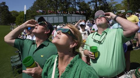 Patrons look up at the sun during an solar eclipse during a practice round in preparation for the Masters golf tournament at Augusta National Golf Club Monday, April 8, 2024, in Augusta, Ga. (AP Photo/George Walker IV)