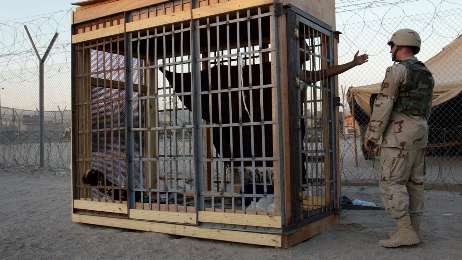 In this June 22, 2004, photo, a detainee in an outdoor solitary confinement cell talks with a military police officer at the Abu Ghraib prison on the outskirts of Baghdad, Iraq. A trial scheduled to begin Monday, April 15, 2024, in US District Court in Alexandria, Virginia, will be the first time that survivors of Abu Ghraib prison will bring their claims of torture to a US jury. Twenty years ago, photos of abused prisoners and smiling US soldiers guarding them shocked the world.