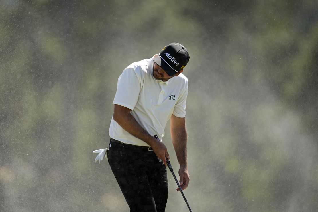 Jason Day shields himself from windswept sand at the 18th hole.