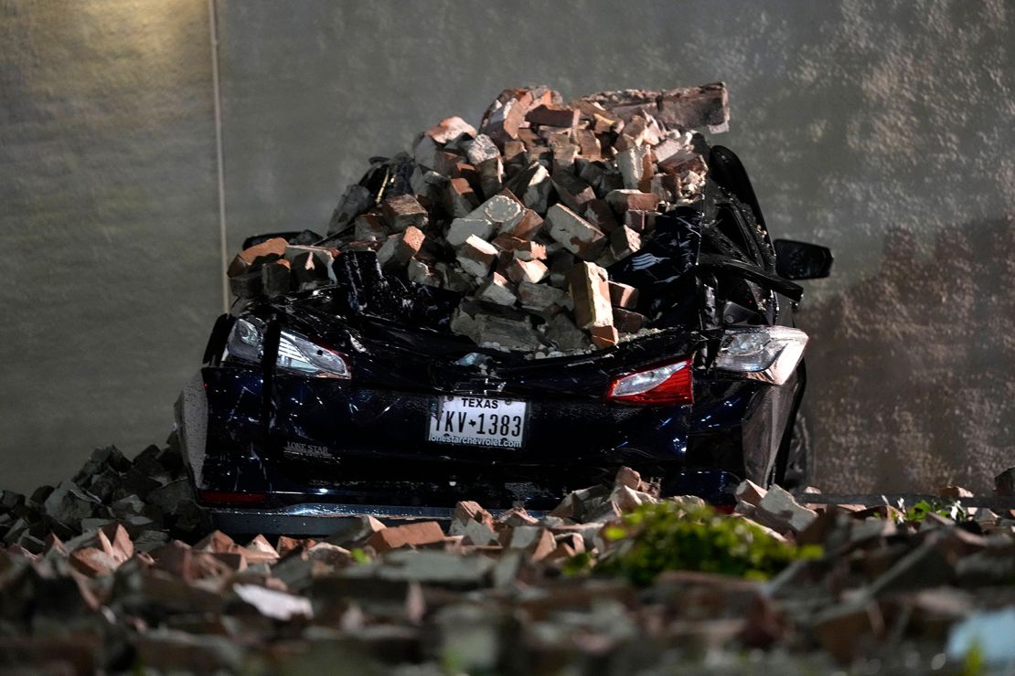A car crushed by bricks from a fallen building wall sits in a downtown parking lot after a severe thunderstorm passed through Thursday in Houston.