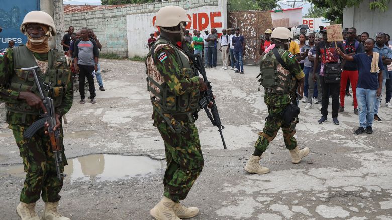 Kenyan police patrol an area near the international airport as a man holds a sign with a welcome message and a plea for jobs, in Port-au-Prince, Haiti, Wednesday, July 3, 2024. (AP Photo/Odelyn Joseph)