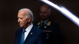 President Joe Biden is seen against a dark background, with a somber expression. 