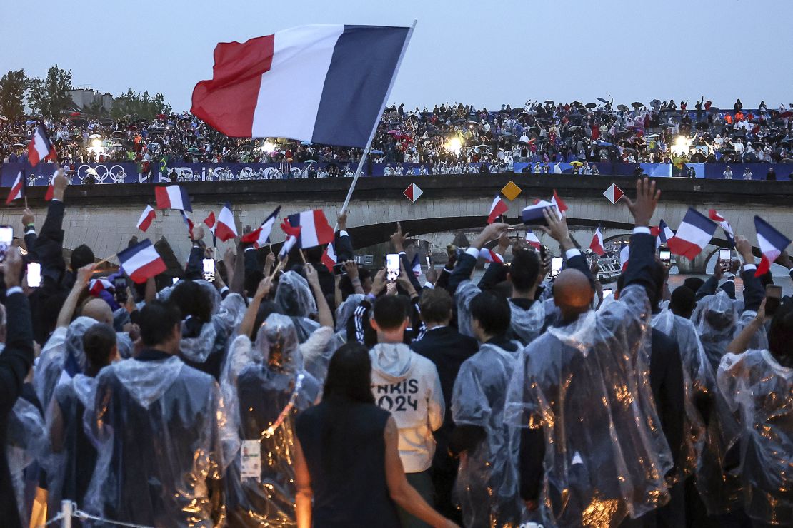 French athletes wave flags as they sail in a boat on the river Seine during the opening ceremony for the 2024 Summer Olympics in Paris, France, Friday, July 26, 2024.