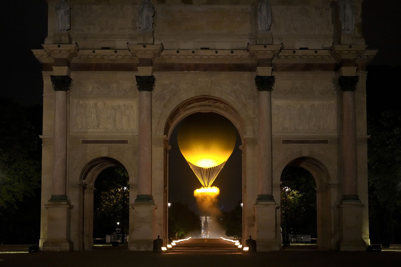 The lit Olympic cauldron can be seen in the air through the Arc de Triomphe du Carrousel.