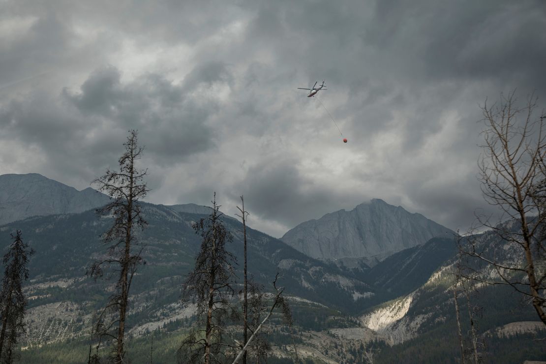 A helicopter buckets water onto smoldering fires outside of Jasper, Alberta, Canada, on Friday. Wildfires encroaching into the townsite of Jasper forced an evacuation of the national park.