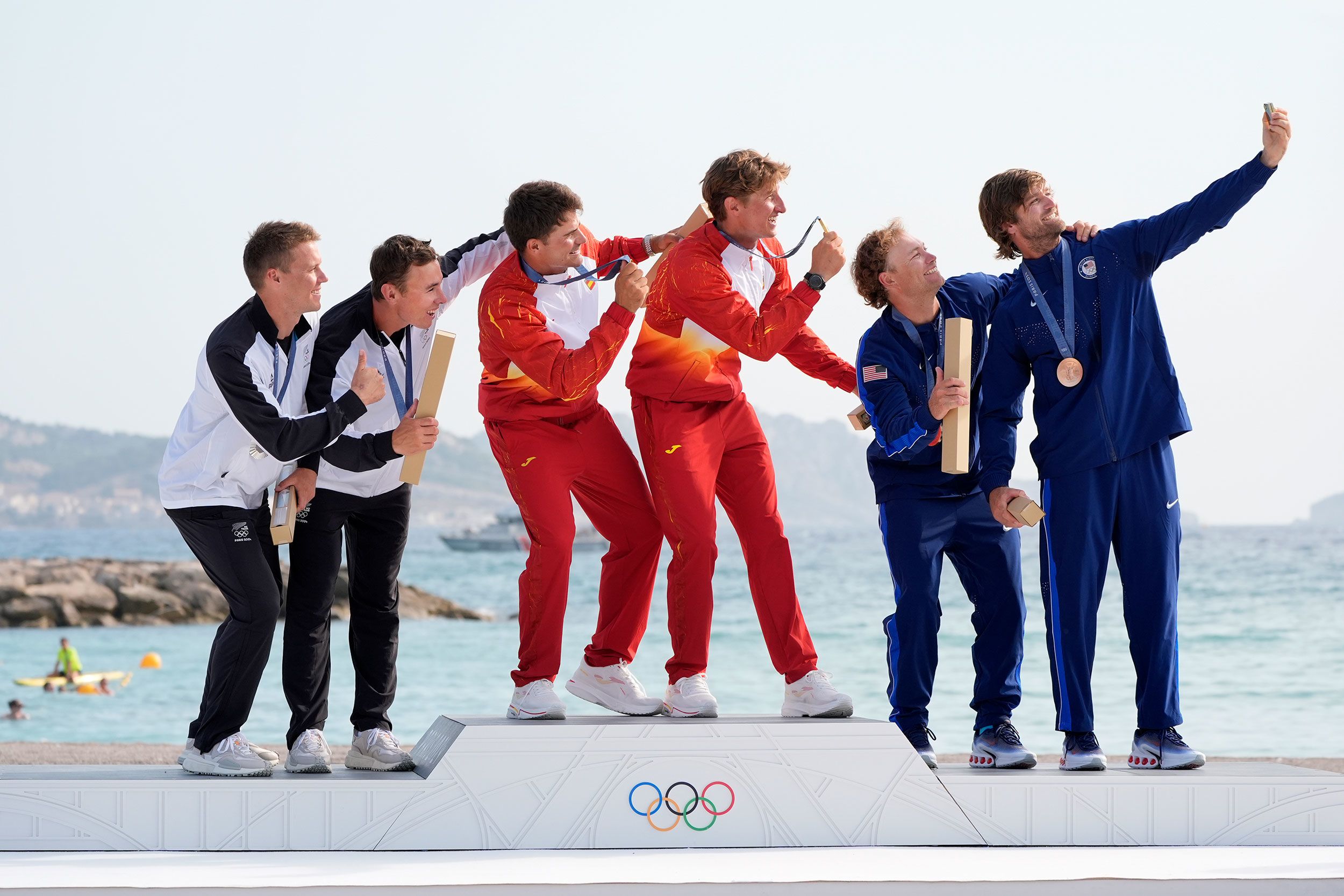 From left, New Zealand's Isaac McHardie and William McKenzie, Spain's Diego Botín and Florián Trittel, and the United States' Ian Barrows and Hans Henken take a group selfie on the medal podium after a sailing event on August 2.