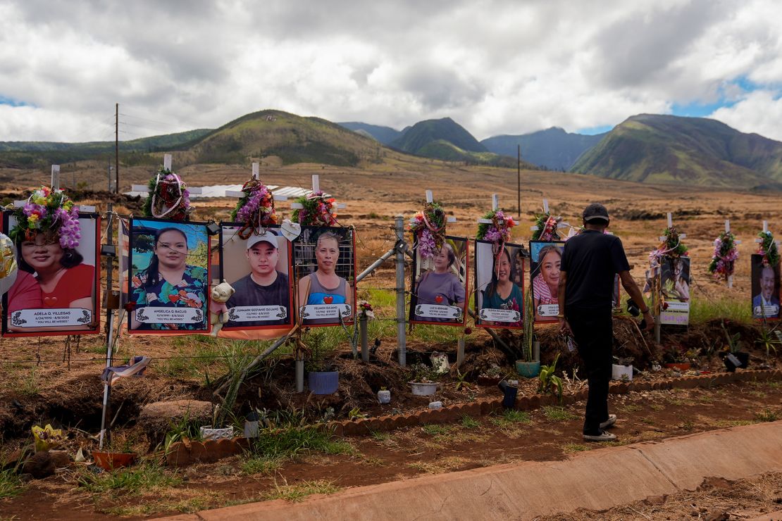 A visitor walks by photos of victims of the August 2023 wildfire at a memorial near the Lahaina Bypass highway on July 6, 2024. Tourists are grappling with how to respectfully visit the area where so much devastation and loss occurred just one year earlier.