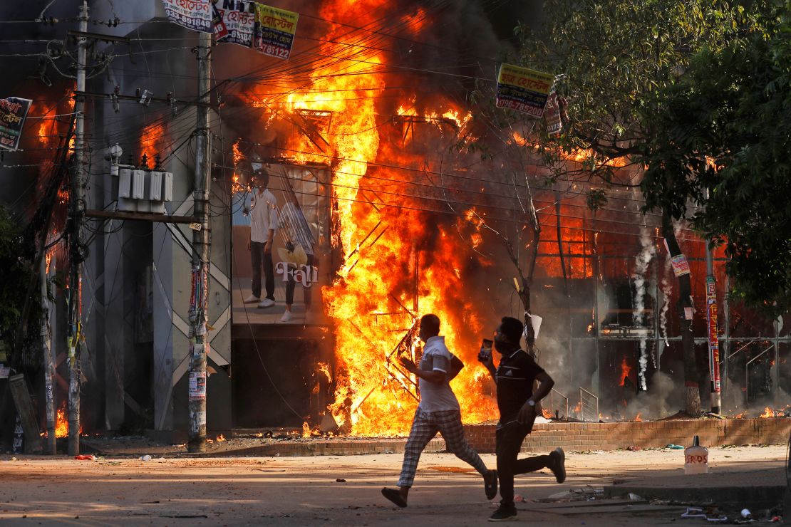 Men run past a shopping center which was set on fire by protesters during a rally against Prime Minister Sheikh Hasina and her government in Dhaka, Bangladesh, on August 4, 2024.