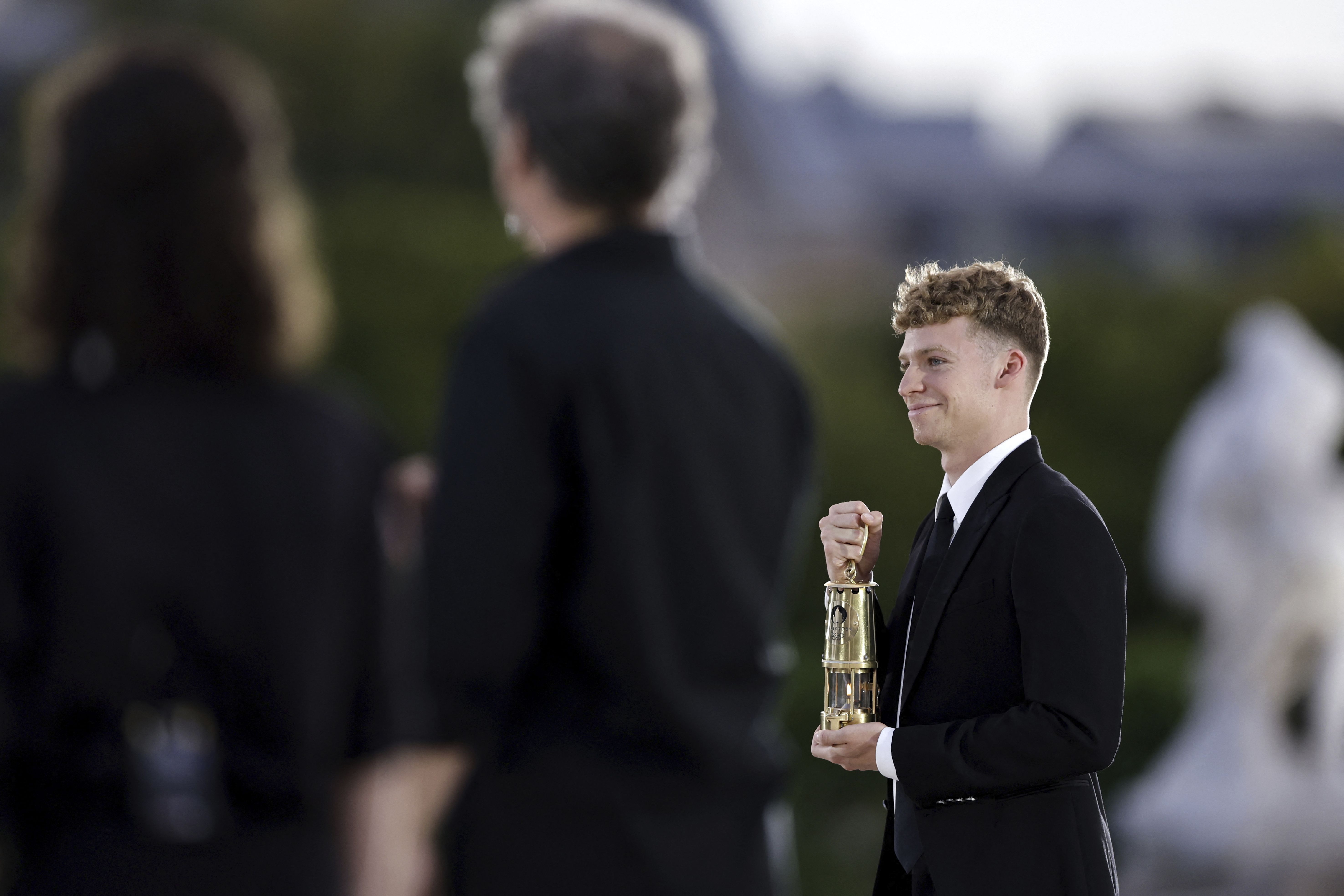 French swimmer Léon Marchand carries the Olympic flame at the Tuileries Garden in Paris.