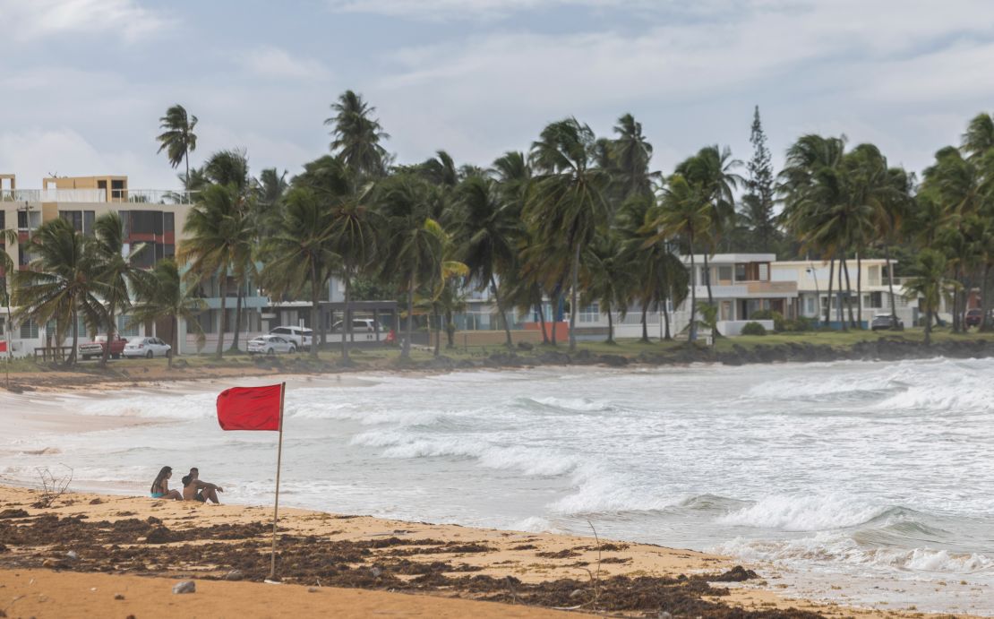 Tourists sit on La Pared Beach as Tropical Storm Ernesto churns up the surf near Luquillo, Puerto Rico, on Tuesday.