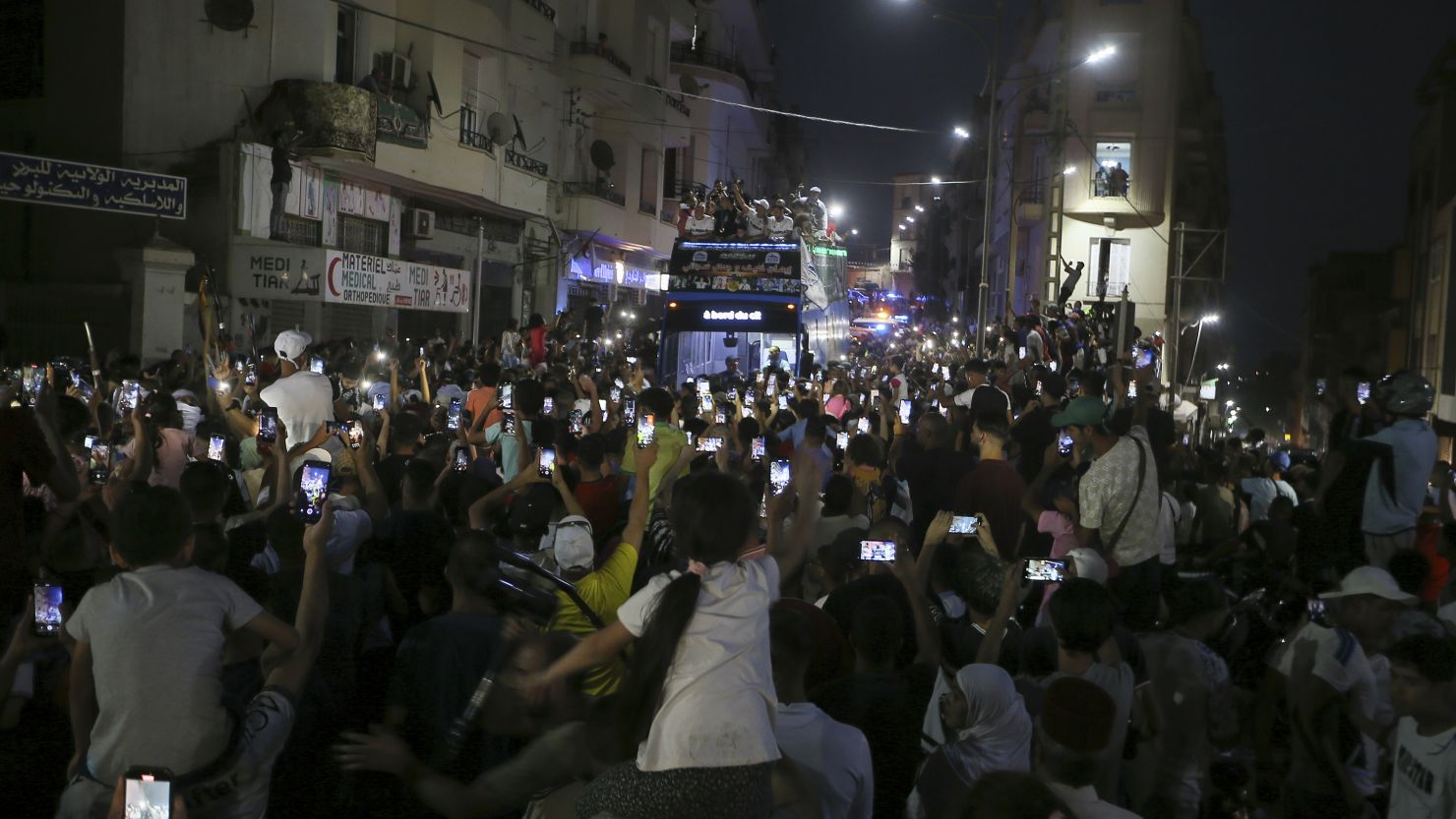 People gather in the streets as Olympic gold medalist Imane Khelif waves from the top of a double decker bus.