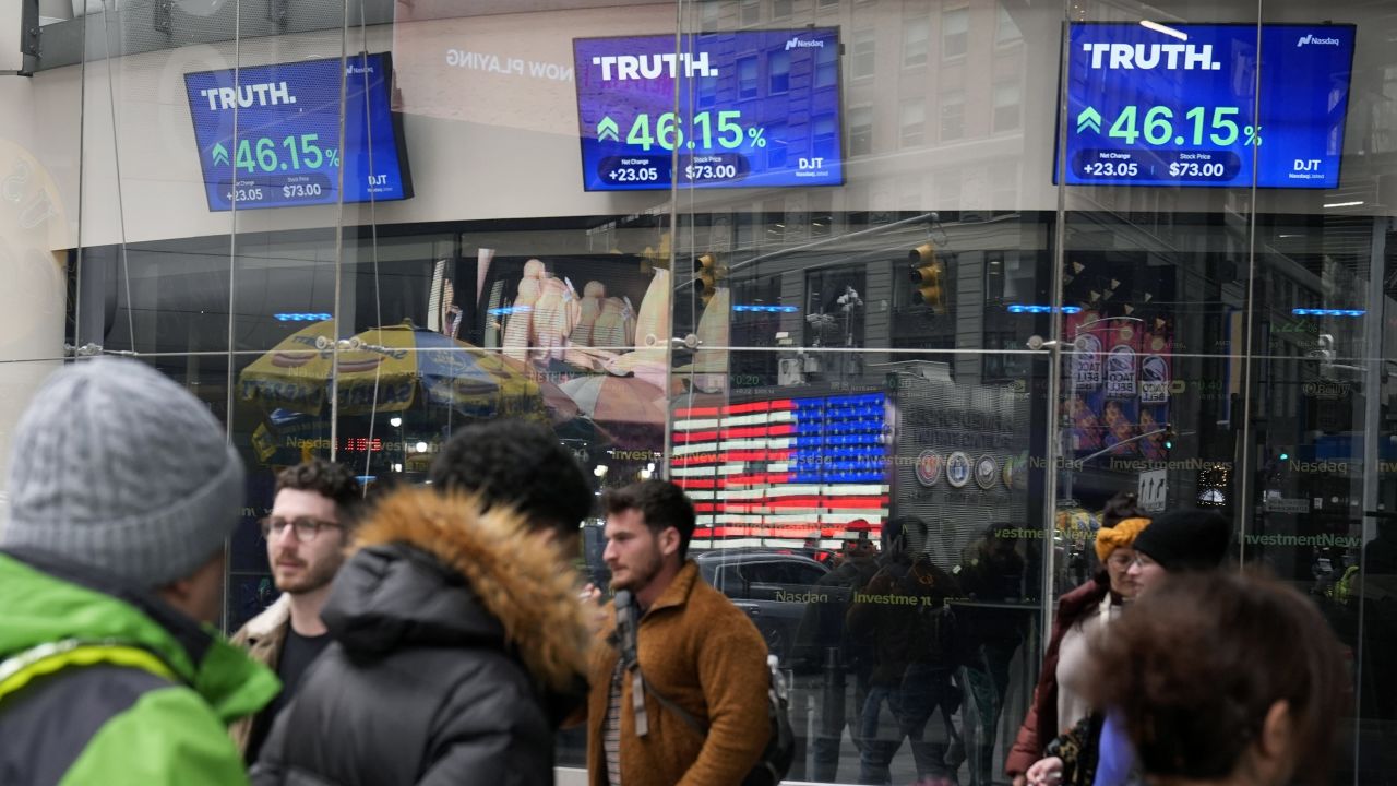 Pedestrians walk past the Nasdaq building as the stock price of Trump Media & Technology Group Corp. is displayed on screens in March 2024 in New York.