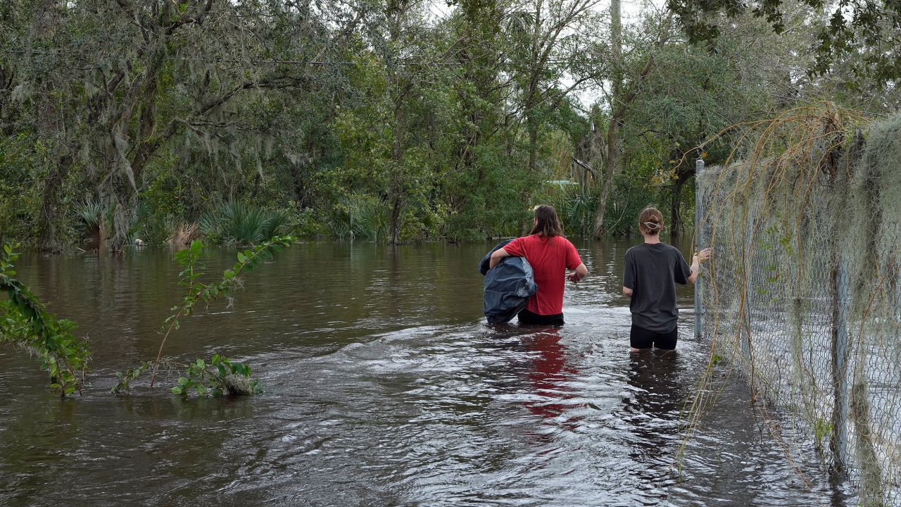 Connor Hughes and Kaylee Swenson walk through floodwaters from the Alafia River on Friday in Lithia, Florida.