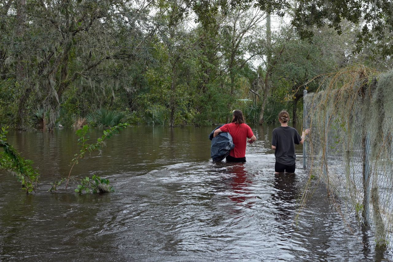 Connor Hughes and Kaylee Swenson walk through floodwaters from the Alafia River on Friday in Lithia, Florida.