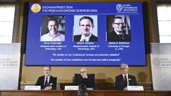 Academy of Sciences permanent secretary Hans Ellegren, center, Jakob Svensson, left, and Jan Teorell, of the Nobel assembly announce the Nobel memorial prize in economics winners, Daron Acemoglu, Simon Johnson and James A Robinson, seen on screen, during a press meeting at the Royal Swedish Academy of Sciences in Stockholm, Sweden, Monday Oct. 14, 2024. (Christine Olsson/TT News Agency via AP)