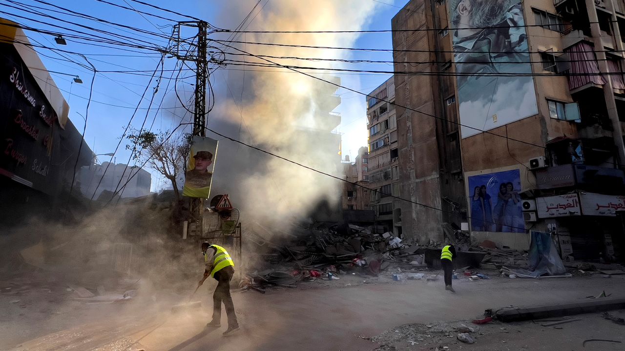 Workers clean a street as smoke rises from a destroyed building that was hit by an Israeli airstrike in Dahiyeh, in the southern suburb of Beirut, Lebanon on October 20.