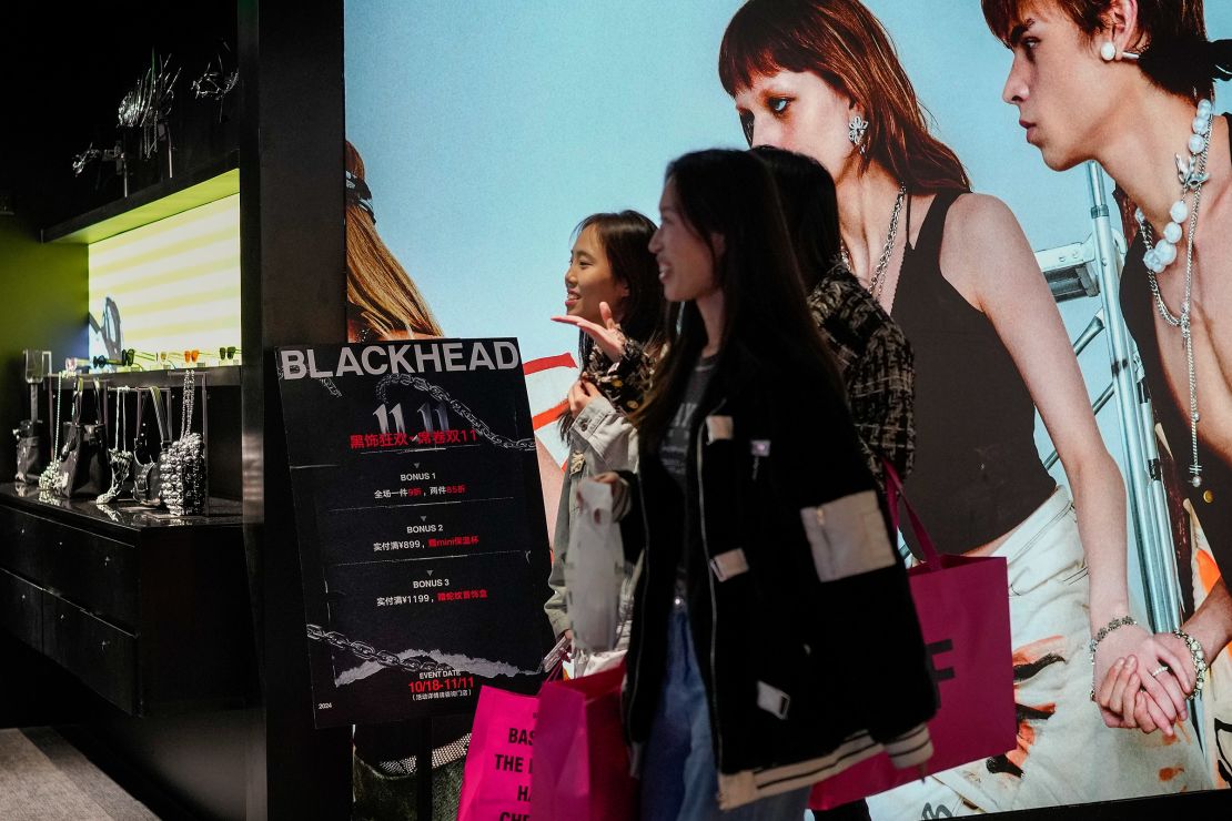 Vrouwen lopen op 11 november 2024 door een winkel voor modeaccessoires met een poster ter promotie van Singles' Day-kortingen in een winkelcentrum in Peking, China.