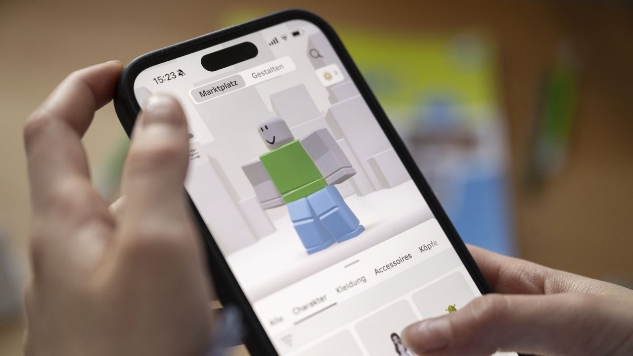 A girl operates a smartphone on which the Roblox app can be seen.