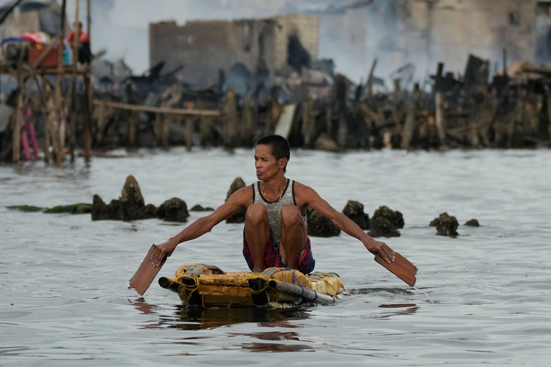 A resident uses an improvised float to check their home while the slum area is still smouldering from the fire in Tondo, Manila.