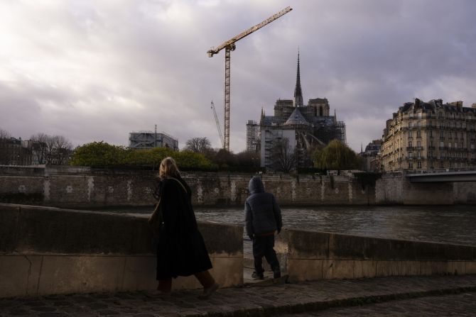 People walk along the banks of the Seine opposite Notre Dame cathedral hours before its formal reopening.