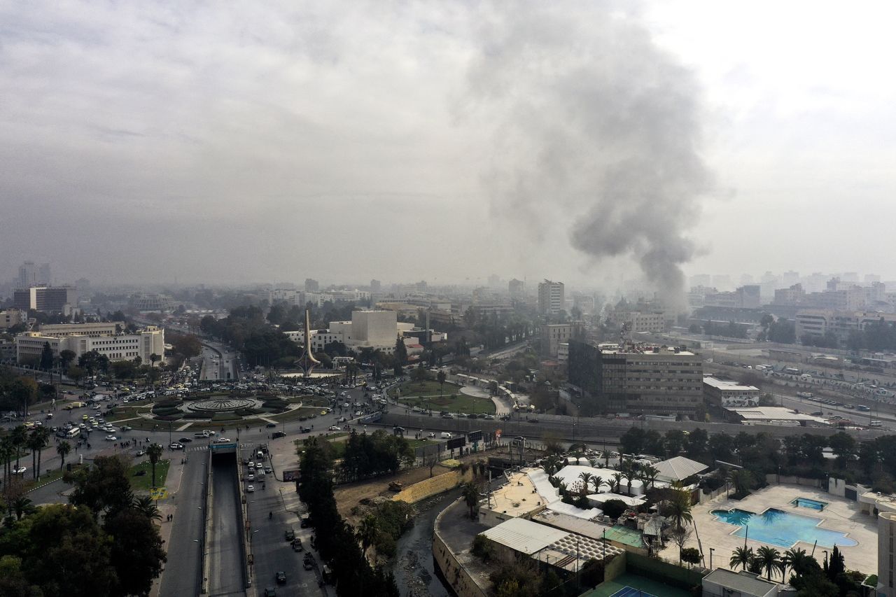 Smoke billows in the background as residents and opposition fighters celebrate in a central square after opposition forces took control of the city in Damascus, Syria, on December 8.