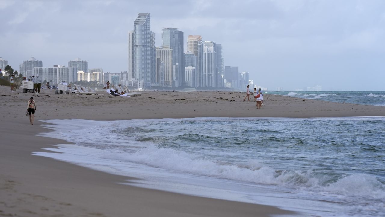 People walk along the beach in Surfside, Fla., near the skyline of Sunny Isles Beach, an area from Miami Beach to Sunny Isles Beach where dozens of beachside high-rise condo and luxury hotel buildings are sinking or settling in unexpected ways, in some cases because of construction in the area from other building projects, according to a new study Tuesday, Dec. 17, 2024. (AP Photo/Lynne Sladky)