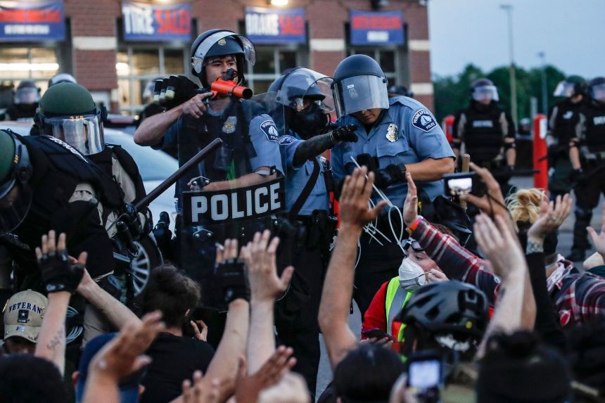A police officer points a hand cannon at protesters who were detained pending arrest in Minneapolis, May 31, 2020, as protests continued following the death of George Floyd.