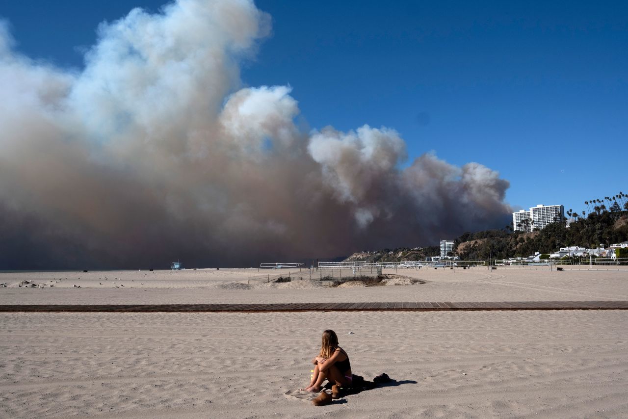 A lone sunbather sits and watches a large plume of smoke rising from the Palisades fire on Tuesday.