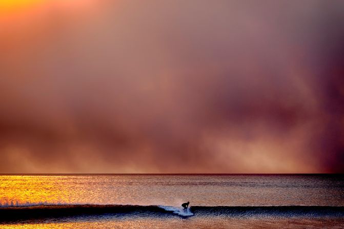 A surfer takes off on a wave in Santa Monica as the sky is blackened from the Palisades Fire.