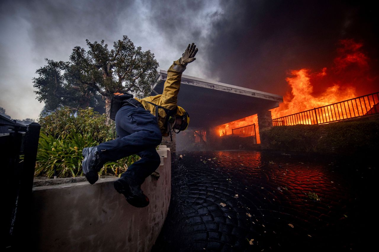 A firefighter jumps over a fence while fighting the Palisades Fire in the Pacific Palisades neighborhood, Los Angeles, on January 7.