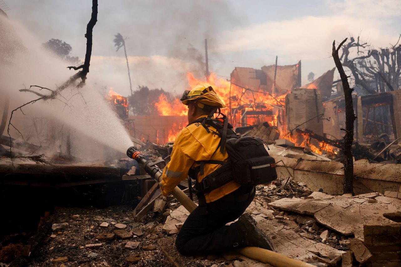 A firefighter battles the Palisades Fire around a burned structure in the Pacific Palisades neighborhood of Los Angeles, on Wednesday, January 8.