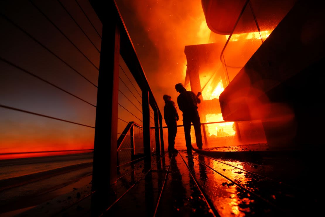 Los bomberos trabajan desde una cubierta mientras el incendio Palisades quema una propiedad frente al mar el 8 de enero en Malibu, California.