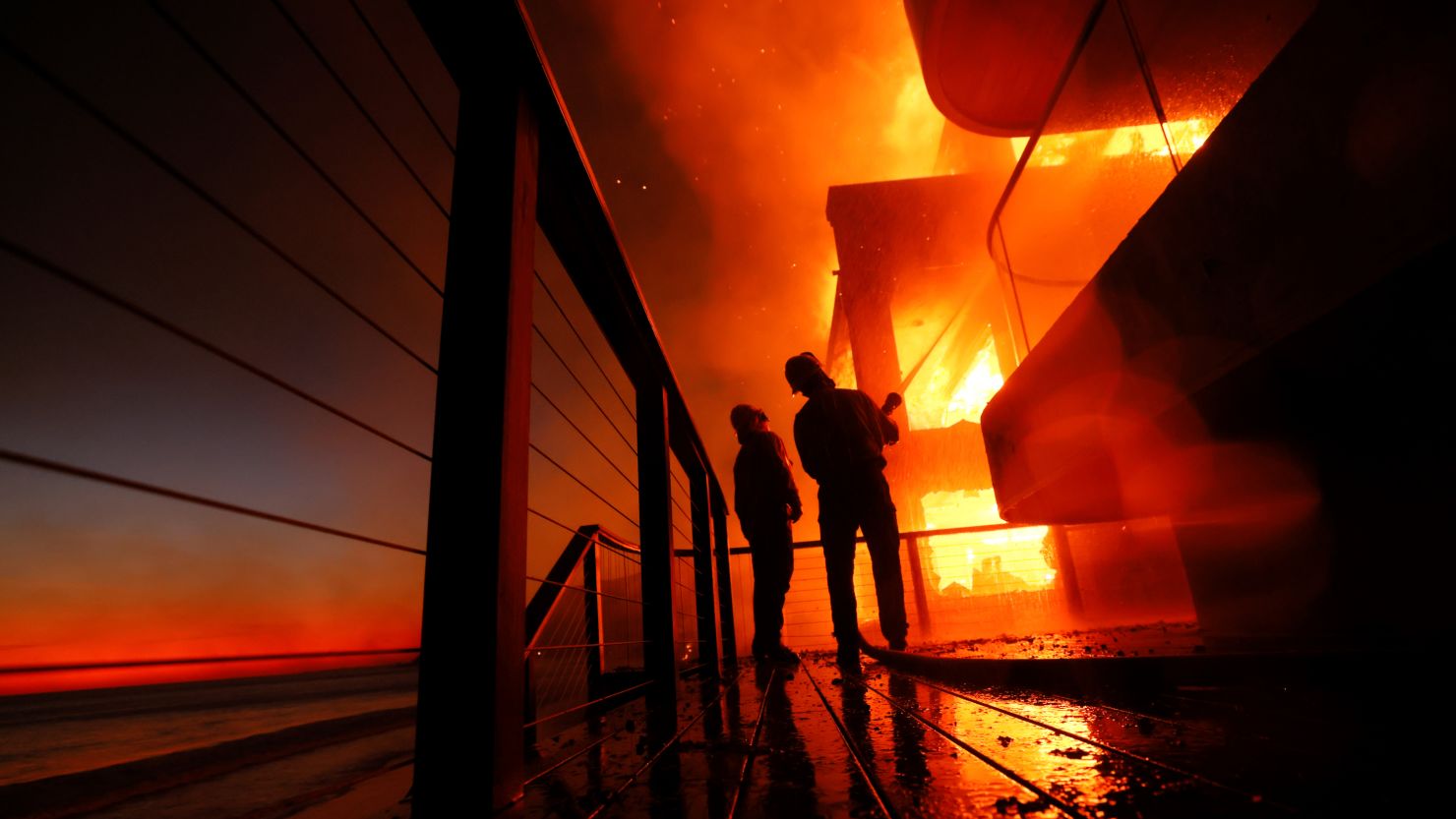 Firefighters work from a deck as the Palisades Fire burns a beachfront property in Malibu on Wednesday.